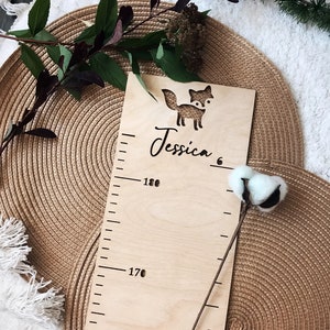 Pu&ograve; includere: Un grafico di crescita in legno con un ritaglio di volpe e il nome "Jessica" scritto su di esso. Il grafico ha segni per l'altezza in centimetri, a partire da 160 cm e fino a 180 cm.