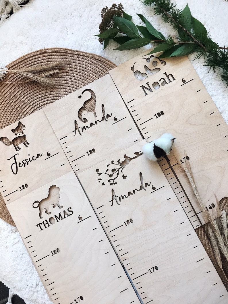 Pu&ograve; includere: Quattro grafici di crescita in legno con ritagli di animali e nomi. I grafici sono in legno chiaro e hanno segni neri per le misurazioni dell'altezza. I nomi sui grafici sono Jessica, Amanda, Thomas e Noah.
