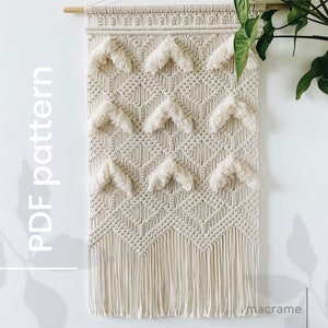 May include: Cream-colored macrame wall hanging with a geometric pattern and fringe. The design features chevron shapes with fluffy accents. The text "PDF pattern" is vertically displayed on the left side of the image.