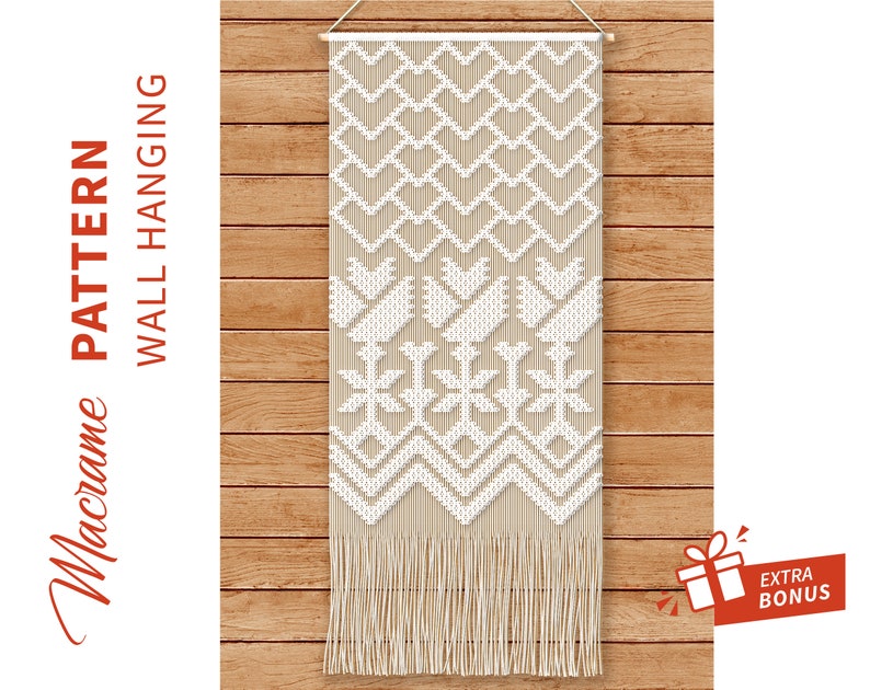 May include: A white macrame wall hanging with a geometric pattern of hearts, flowers, and snowflakes. The hanging is made with natural cotton cord and has a fringe at the bottom.