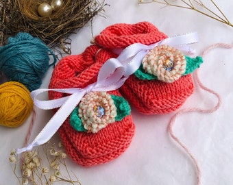 Coral knit baby booties with white crochet roses and green leaves