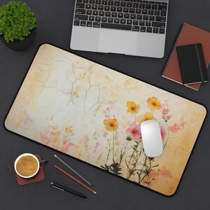 May include: A beige and yellow desk mat with a cracked texture and a watercolour floral design featuring pink and yellow flowers. A white computer mouse is on the mat.