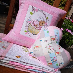 May include: A pink and white patchwork quilt with a pink pillow featuring a hedgehog in a basket and a heart-shaped pillow with a patchwork design of bunnies and flowers.