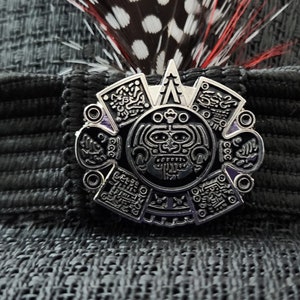 Könnte beinhalten: Eine silberfarbene Metallstifte mit einem schwarzen und violetten Design. Der Stift zeigt ein stilisiertes Gesicht in der Mitte, umgeben von komplizierten Mustern.