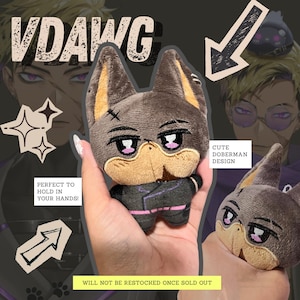 May include: A plush Doberman dog with a cute design, featuring a gray body, tan snout, and pink accents. The text "VDAWG" is at the top. The text "WILL NOT BE RESTOCKED ONCE SOLD OUT" is at the bottom.