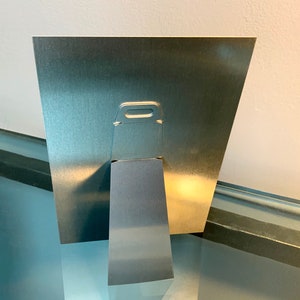 K&ouml;nnte beinhalten: Ein silberner Bilderrahmen aus Metall mit einem eingebauten St&auml;nder auf der R&uuml;ckseite. Der Rahmen hat eine kleine Metallscharniere auf der R&uuml;ckseite zum Aufh&auml;ngen.