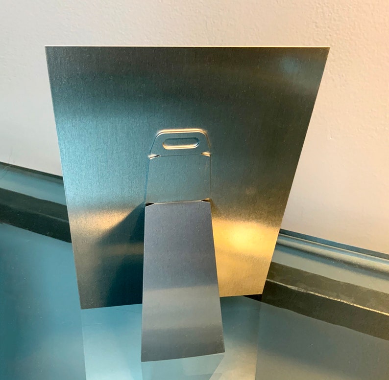 K&ouml;nnte beinhalten: Ein silberner Bilderrahmen aus Metall mit einem eingebauten St&auml;nder auf der R&uuml;ckseite. Der Rahmen hat eine kleine Metallscharniere auf der R&uuml;ckseite zum Aufh&auml;ngen.