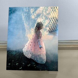 K&ouml;nnte beinhalten: Ein junges M&auml;dchen in einem rosa-wei&szlig;en Kleid mit silbernen Sternen, das vor einem gr&uuml;nen Hintergrund steht.
