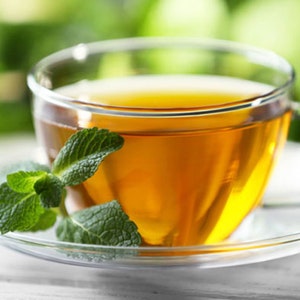 Peut inclure: Une tasse de thé en verre avec une branche de menthe fraîche sur une soucoupe transparente. Le thé est de couleur ambre clair et la menthe est verte.