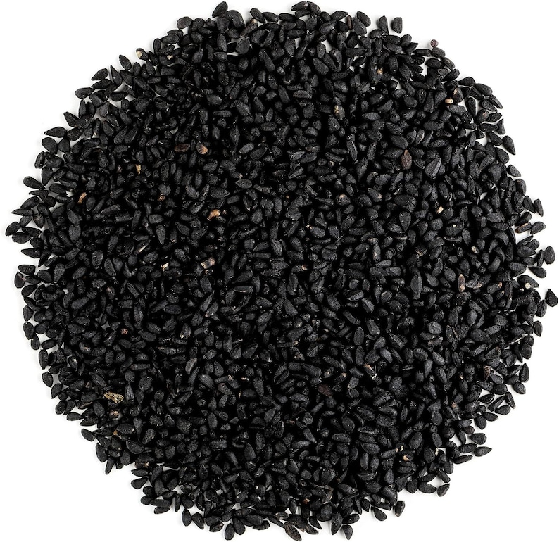 May include: A close-up image of a pile of black seeds against a white background. The seeds are small, oval-shaped, and densely packed together. The seeds have a shiny, smooth texture and a dark, uniform color.