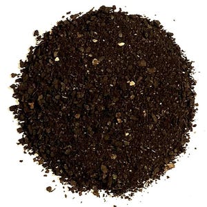 May include: A circular pile of dark brown, coarse-textured granules. The material consists of small, irregular, jagged particles with a matte finish and occasional lighter tan flecks scattered throughout the dark, earthy-toned mixture.