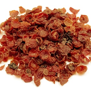 May include: A pile of dried rose hips, showcasing a deep reddish-brown color. The rose hips have a wrinkled texture and varying shapes, with some appearing whole and others broken. The background is plain white, highlighting the natural color of the rose hips.