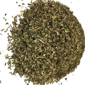 May include: A pile of dried, finely chopped green herbs with varying shades of dark and light olive green leaves. The texture appears coarse and crumbly, consisting of small, irregular leaf fragments scattered in a loose, rounded mound.