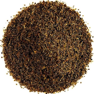 May include: A circular pile of finely ground, dark brown dried herbs and spices. The texture is coarse and granular, featuring a mix of small dark leaf fragments, tiny seeds, and fibrous particles arranged in a dense, uniform mound against a white background.