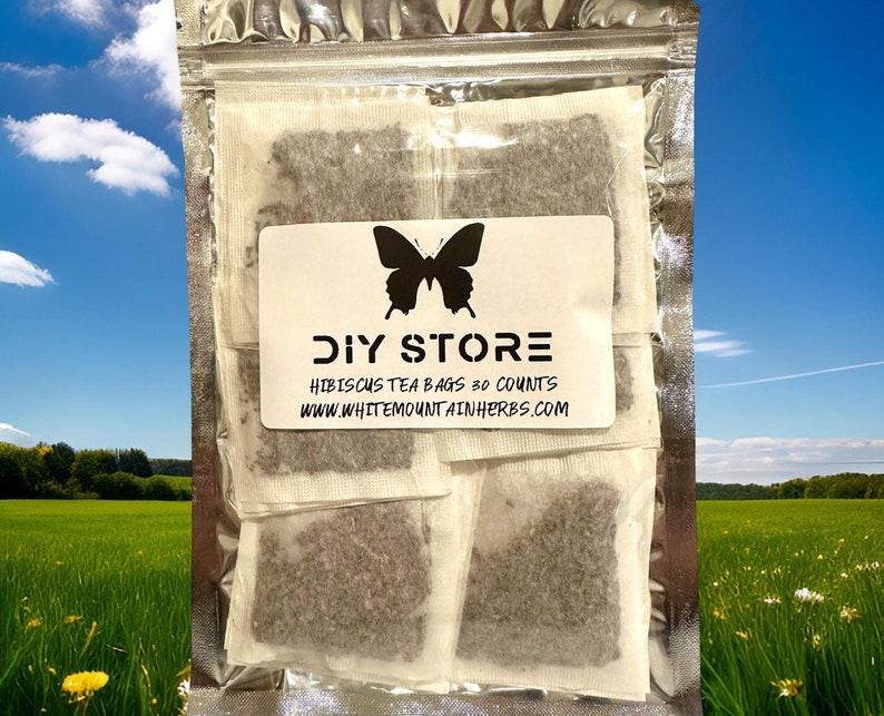 Op de afbeelding: Een witte hersluitbare zak met een vlinderlogo en de tekst "DIY STORE" erop gedrukt. De zak bevat 30 individuele theezakjes met hibiscus thee. De tekst "HIBISCUS TEA BAGS 30 COUNTS" en "WWW.WHITEMOUNTAINHERBS.COM" staat op de zak gedrukt.