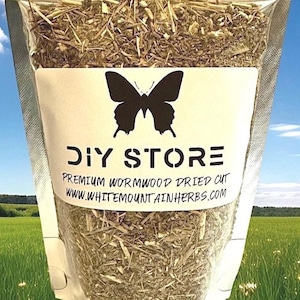 May include: A clear plastic bag filled with dried wormwood herbs. The bag has a white label with a black butterfly logo and the words "DIY STORE" and "PREMIUM WORMWOOD DRIED CUT". The background shows a blue sky and a green field.