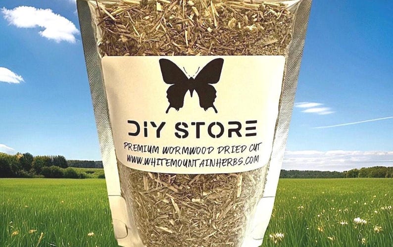 May include: A clear plastic bag filled with dried wormwood herbs. The bag has a white label with a black butterfly logo and the words "DIY STORE" and "PREMIUM WORMWOOD DRIED CUT". The background shows a blue sky and a green field.