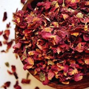 May include: A wooden bowl filled with dried rose petals. The petals are a mix of deep red and faded yellow, with some scattered outside the bowl. The image is taken from a high angle, showing the texture and color of the petals.