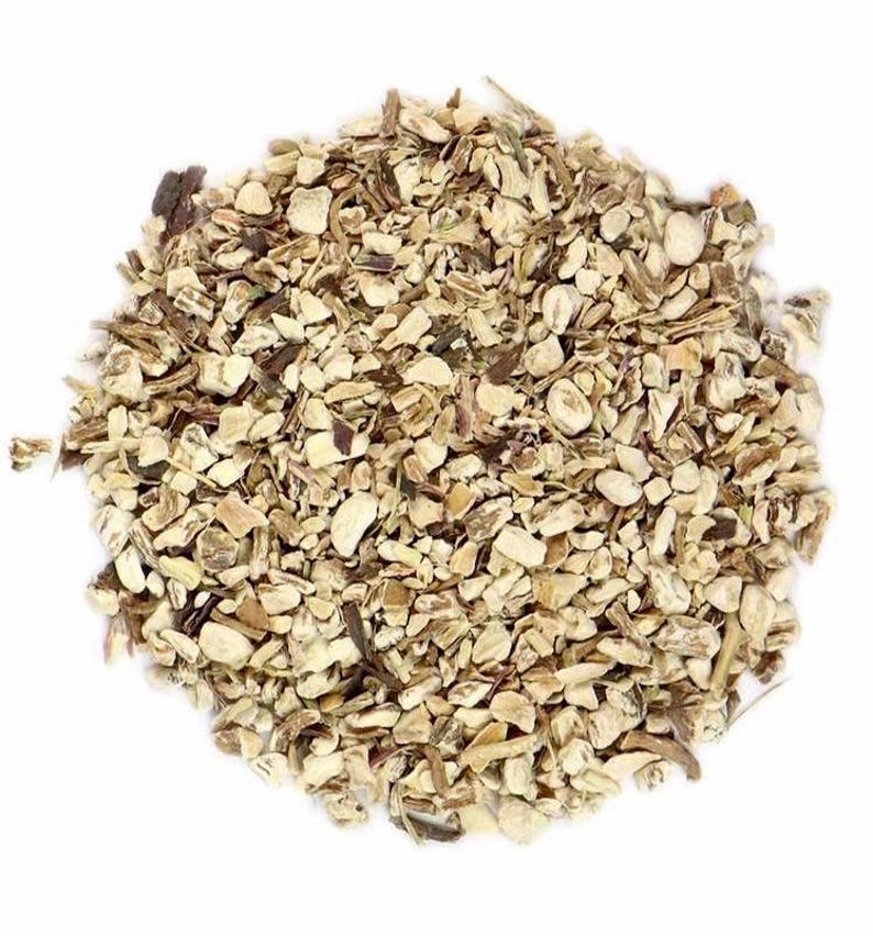 May include: A pile of dried, chopped dandelion root pieces. The organic material consists of small, irregular, beige and light brown fragments with a woody texture, arranged in a circular mound against a plain white background.