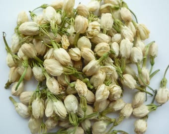 May include: A close-up shot of dried jasmine buds. The buds are off-white with green stems, and they are densely packed together. The image is well-lit, highlighting the texture and details of the dried flowers.