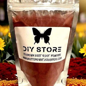 May include: A silver pouch filled with premium beet root powder. The pouch has a white label with a black butterfly and the words "DIY STORE". The background features yellow flowers and red and yellow foliage.