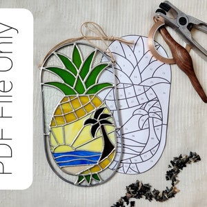 May include: A stained glass pineapple with a palm tree and sunset scene. The image also shows a pattern for the stained glass project, tools for making stained glass, and a pile of glass pieces.