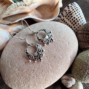 Può includere: Un paio di orecchini d'argento con un design delicato e intricato. Gli orecchini hanno la forma di una mezzaluna con un motivo a spirale e piccole perline attorno al bordo. Sono appesi a un gancio d'argento.
