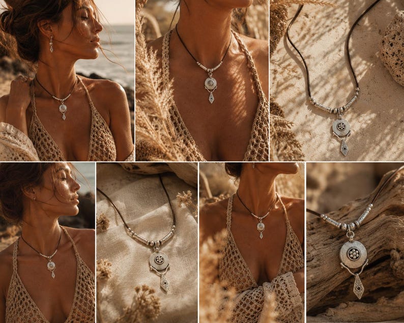 May include: A silver pendant necklace featuring a circular centerpiece with a floral motif, suspended from a dark cord with silver accents. The pendant includes a dangling geometric element with a small dark stone, creating a layered look.
