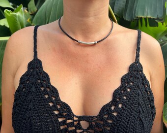 May include: A black leather choker necklace with a silver bar pendant. The necklace is worn by a person with a black crocheted top.