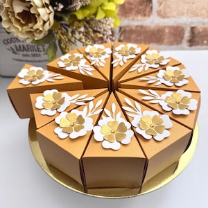 May include: A golden-yellow, pie-shaped gift box set. Each slice is decorated with white and gold floral embellishments. The boxes are arranged on a gold-colored, circular base, creating a decorative presentation for special occasions.