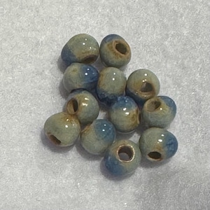 May include: A collection of ceramic beads in shades of blue and green. Each bead has a hole running through the center, and a glossy finish. The beads are round and appear to be handmade, perfect for jewelry making.