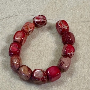 May include: A strand of red and maroon square beads. The beads are strung together on a thin, clear wire. The beads have a glossy finish and a marbled appearance.