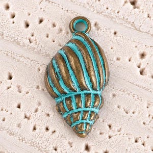 May include: A seashell-shaped pendant charm featuring a metallic bronze finish with recessed areas highlighted in a vibrant turquoise blue color. The charm has a circular loop at the top for attachment and displays a detailed, ridged spiral texture.