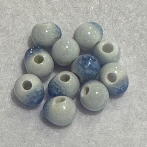 Puede incluir: Un conjunto de cuentas de cerámica azul claro y blanco con efecto marmolado. Cada cuenta tiene un agujero en el centro para ensartar. Las cuentas tienen un acabado brillante y el veteado azul varía ligeramente.