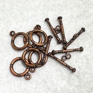 May include: A collection of copper-toned metal toggle clasps, each consisting of a circular ring and a matching T-bar component. The pieces feature a textured, ribbed design along their surfaces, providing a consistent look for jewelry making.