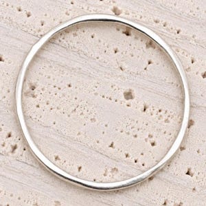 May include: A thin, circular silver-colored metal ring with a smooth, polished finish. The band has a consistent, slender width throughout its entire circumference, creating a simple and clean geometric shape without any additional embellishments.