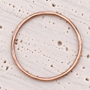 May include: A thin, circular ring with a warm, metallic copper-toned finish. The band features a smooth, rounded profile with a consistent thickness throughout its circumference, showcasing a polished surface that reflects light evenly across the metal.