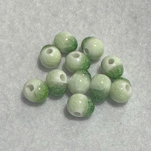 Könnte beinhalten: Eine Ansammlung hellgrüner und weißer Perlen mit einem gesprenkelten Muster. Jede Perle hat ein Loch in der Mitte. Die Perlen sind rund und scheinen aus einem glatten Material zu bestehen.