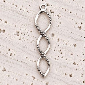 May include: A silver-toned metal jewelry charm featuring a vertical, elongated, twisted infinity-like design. The charm consists of three interconnected open loops with a textured, beaded edge along the outer frame and a small circular loop at the top.