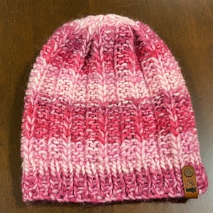 May include: Pink and white striped knitted beanie with a brown leather tag.