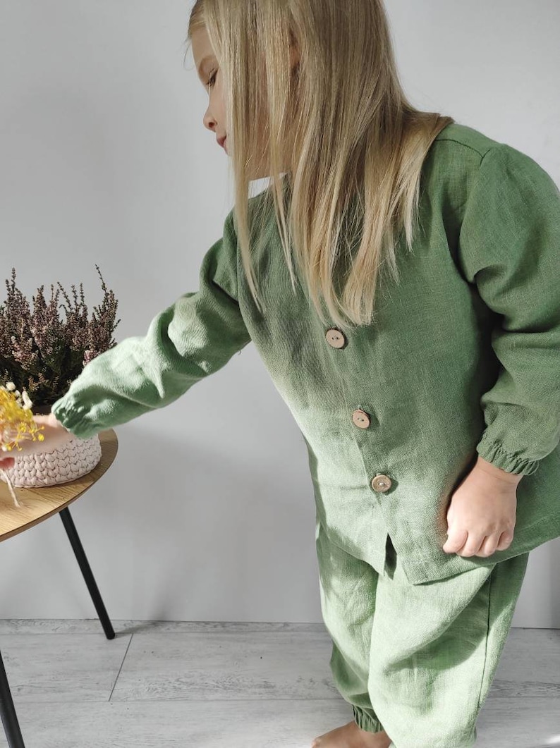 Puede incluir: Un conjunto de camisa de manga larga color verde salvia con botones y pantal&oacute;n a juego. La camisa presenta tres botones grandes, redondos y de madera clara en la parte delantera, adem&aacute;s de pu&ntilde;os el&aacute;sticos. El pantal&oacute;n tiene una cintura el&aacute;stica.