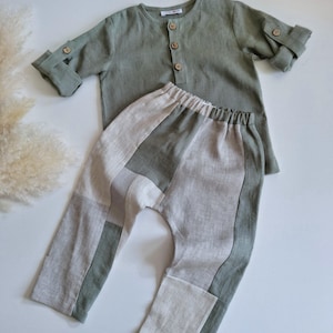 Puede incluir: Una camisa de manga larga color verde salvia con tapeta de botones y mangas con trabillas, combinada con pantalones de bloques de color con paneles alternos de tela verde salvia y beige claro. La camisa tiene una pequeña etiqueta blanca.