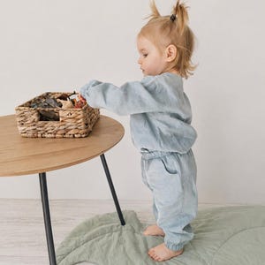 Puede incluir: Un conjunto de color azul claro compuesto por una camiseta de manga larga y pantalones a juego con cintura el&aacute;stica, confeccionado en un tejido texturizado. El conjunto presenta un corte holgado con pu&ntilde;os fruncidos en mu&ntilde;ecas y tobillos.
