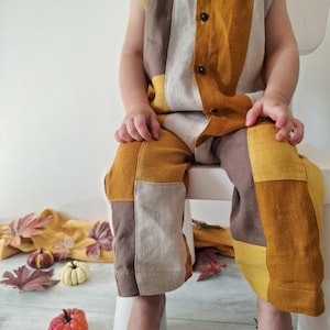 Könnte beinhalten: Ein ärmelloser Jumpsuit mit einem Color-Block-Muster aus senfgelben, braunen und beigen Stoffbahnen. Das Kleidungsstück hat einen Rundhalsausschnitt und eine Knopfleiste vorne mit dunklen Knöpfen, die bis zu den langen Hosenbeinen reicht.