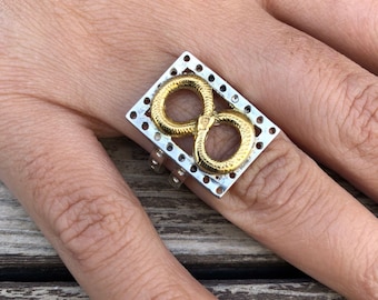 May include: A silver ring with a gold infinity symbol design. The ring is made of two metals and has a unique, modern look.