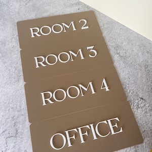 Op de afbeelding: Vier bruine rechthoekige borden met witte letters. De borden geven "ROOM 2", "ROOM 3", "ROOM 4" en "OFFICE" aan.