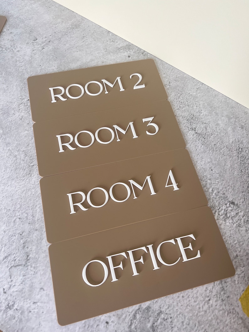 Op de afbeelding: Vier bruine rechthoekige borden met witte letters. De borden geven "ROOM 2", "ROOM 3", "ROOM 4" en "OFFICE" aan.
