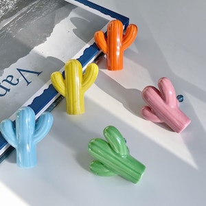 May include: Five ceramic cactus-shaped drawer pulls in different colours: blue, yellow, green, orange and pink.