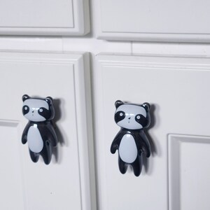 May include: Two black and white panda bear drawer pulls with a glossy finish. The panda bears have black eyes and a white belly.