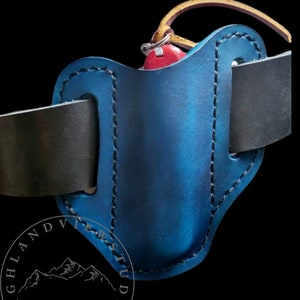 May include: A blue leather belt holster with a red and silver pocket knife. The holster is stitched with black thread and has a black leather belt strap. The holster is labeled "HIGHLAND VIE W STUDIO" and "Sutton, NH".